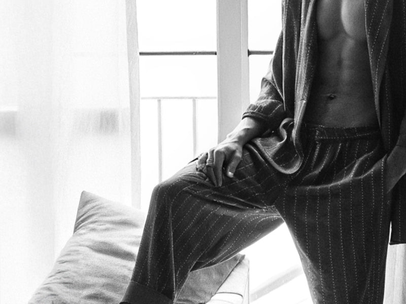 Homme debout près d'une fenêtre vêtu d'un pyjama SLAZZ à rayures, ambiance lumineuse en noir et blanc